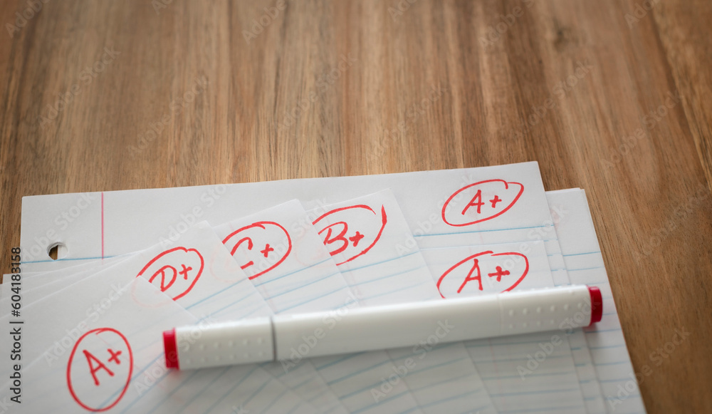Different grades school paper marked in red ink over a wood desktop. Test results concept. Pass exam.
